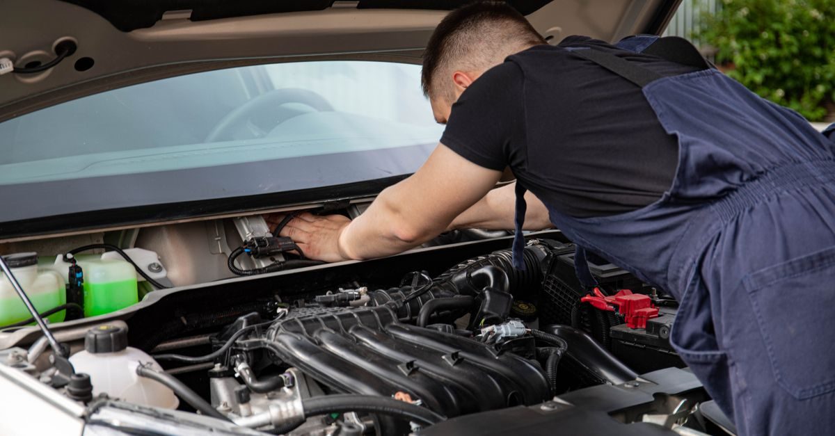 An auto mechanic performing engine maintenance under the hood of a car