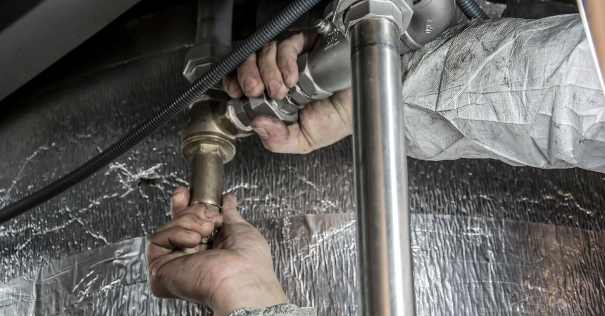 A tradesperson working on pipework with hand tools