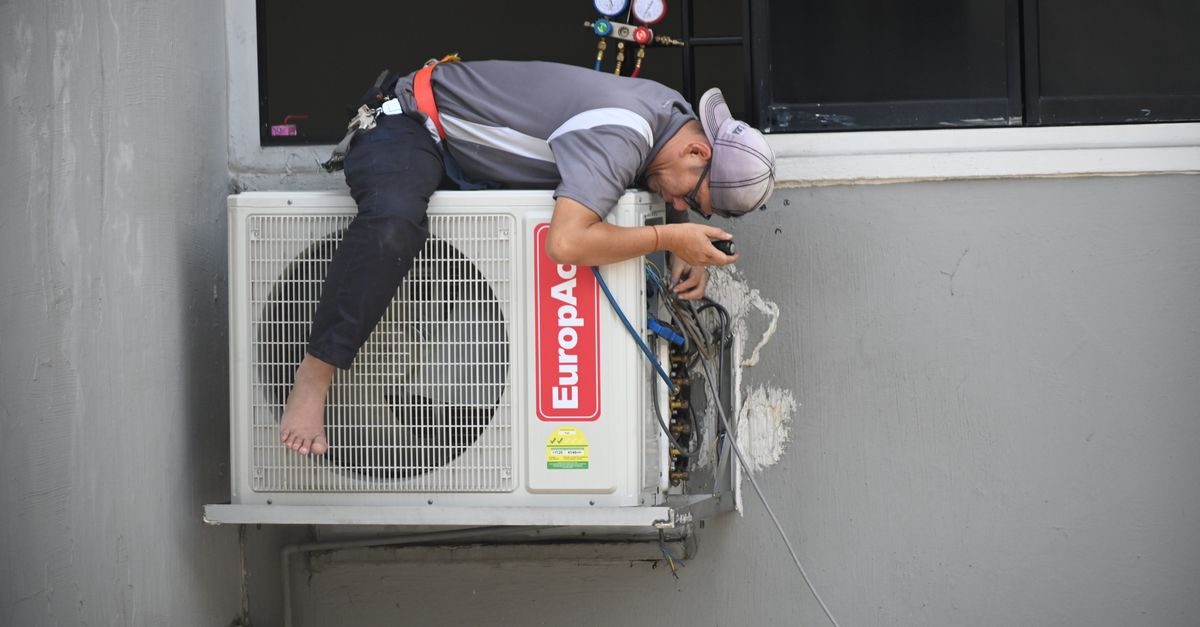 A technician repairing an outdoor air conditioning unit mounted on a building