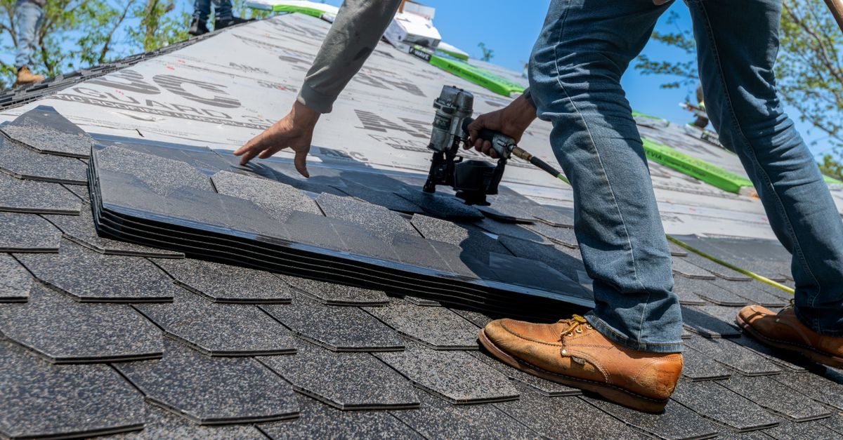 A roofer using a nail gun to install shingles on a residential roof